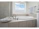 Bright bathtub beneath a window in a tile surround, near a frameless shower and white storage cabinet at 8075 S Vandriver Way, Aurora, CO 80016