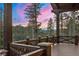 An elevated balcony with wooden railings offers stunning views of the surrounding forest and mountain landscape at sunset at 30 W Ranch Trl, Morrison, CO 80465