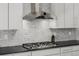 Close up of a gas range and exhaust hood above it, complemented by white cabinets and subway tile backsplash at 3059 Morningbird Ln, Castle Rock, CO 80109