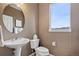 Cozy powder room with a pedestal sink, toilet, round mirror, and a window providing natural light at 14682 W Amherst Pl, Lakewood, CO 80228