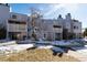 Exterior view of a multi-story condominium with a balcony, stairs, and lawn covered in snow at 7665 E Eastman Ave # 107B, Denver, CO 80231