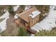 Aerial view of a brown two-story home with a large deck, walk out basement and snowy landscape at 25019 N Mountain Park Dr, Evergreen, CO 80439