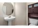 Half-bath with pedestal sink, oval mirror, and dark wood storage cabinet over toilet at 19240 E Carolina Dr # 104, Aurora, CO 80017
