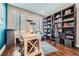 A well-lit office features hardwood floors, built-in bookshelves with a ladder, a cozy chair, and a wooden desk at 10178 Nadine Ave, Parker, CO 80134