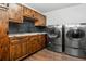Well-equipped laundry room with wood cabinetry, stone backsplash, sink, and modern washer and dryer units at 12570 W 60Th Ave, Arvada, CO 80004