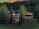 Exterior of a gray stone home with lit windows during sunset amongst lush trees at 2191 Baldy Ln, Evergreen, CO 80439
