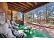 Inviting covered porch with comfortable seating, wood beams, and a view of the bocce ball court and the surrounding woods at 2851 Interlocken Dr, Evergreen, CO 80439