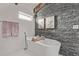 Modern bathroom featuring a soaking tub, a grey stone accent wall, and natural light at 745 S Eliot St, Denver, CO 80219