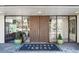 Building entrance with double doors, glass sidelights, planters, and doormat that reads, 