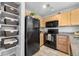 Kitchen featuring light wood cabinets, black appliances, and wall display shelving for storage at 6001 S Yosemite St # H204, Greenwood Village, CO 80111