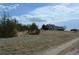 A two-story tan home with a white fence sits on a hill with a gravel driveway in the foreground at 74500 E 136Th Ave, Byers, CO 80103
