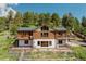 Two-story log cabin with multiple balconies and decks, set in a lush, green, wooded landscape at 12135 Cochise Cir, Conifer, CO 80433