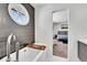 Modern bathroom featuring a soaking tub with gray tiled accent wall and round window at 7918 S Depew St # D, Littleton, CO 80128