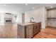 Modern kitchen island with stainless steel appliances and light wood flooring, flowing into a living space with a fireplace at 6882 Oak Canyon Cir, Castle Pines, CO 80108
