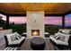 Relaxing outdoor living area with a stone fireplace, comfortable seating, and wooden ceiling with sunset views at 15191 Dinosaur Ridge Rd, Morrison, CO 80465