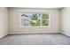 A bright bedroom featuring neutral walls and carpet, and a large window overlooking lush greenery and the neighboring houses at 3823 Horiuchi St, Brighton, CO 80601