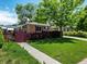 Charming brick home features lush green lawn, mature shade tree, and red picket fence at 3580 Krameria St, Denver, CO 80207
