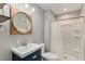 A bathroom featuring a shower, toilet, sink with a round mirror, and a wooden shelf at 5102 S Lisbon Way, Centennial, CO 80015