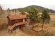 An exterior elevation of a two-story home with a deck, a pergola, mature trees and wood siding at 26167 De Berry St, Conifer, CO 80433