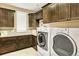Well-lit laundry room features front-load washer and dryer and plenty of dark wood cabinet storage and counter space at 9164 E Lost Hill Trl, Lone Tree, CO 80124