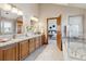 Bright bathroom featuring double vanity with granite counters, wood cabinets, and a view into the bedroom at 15935 W 77Th Pl, Arvada, CO 80007
