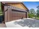 Attached two-car garage with a modern brown door, wooden beam siding, and exterior light fixture, with house number displayed at 776 Hilltop Rd, Palmer Lake, CO 80133