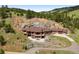 Aerial view of luxury home nestled in wooded hills featuring stone terraces and ample parking at 21609 Clarence Ln, Golden, CO 80401