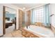 Bright bathroom features a tiled tub, glass-enclosed shower, and view into the main bedroom at 2753 E 139Th Dr, Thornton, CO 80602
