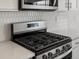 A close-up of a stainless steel gas range with a tile backsplash and microwave above it at 1975 S Coolidge Way, Aurora, CO 80018