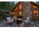 Log cabin home with stone chimney, outdoor patio, fire pit, and seating area amidst mountain scenery at 80 Spruce Ct, Evergreen, CO 80439