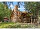 Charming log cabin with stone chimney, surrounded by trees, offering a rustic and inviting appeal at 80 Spruce Ct, Evergreen, CO 80439