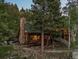 Exterior of a log cabin with a stone chimney and an outdoor patio amidst a tranquil forest at 80 Spruce Ct, Evergreen, CO 80439