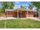 Exterior view of backyard showcasing a brick house, grass and partial covered patio at 7192 W 67Th Pl, Arvada, CO 80003
