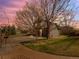 Charming home features a two-car garage, green lawn, and mature trees against a picturesque sunset sky at 11910 W 83Rd Pl, Arvada, CO 80005