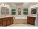 Bright bathroom featuring double vanities, a soaking tub, tile floors, and views of the landscaped yard at 6402 Wauconda Dr, Larkspur, CO 80118