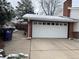 Spacious two-car garage with ample driveway space and brick detailing. Partially covered in snow at 3770 S Ulster St, Denver, CO 80237