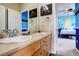 Well-lit bathroom with double sinks, wooden cabinetry, and a view into a stylishly decorated bedroom at 14200 W 86Th Pl, Arvada, CO 80005