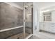 Bathroom with tiled shower, bench, and double vanity with white cabinets and luxury vinyl plank flooring at 9277 Truckee Ct, Commerce City, CO 80022
