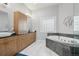 Bathroom featuring double sinks, wooden cabinets, a soaking tub, and a glass block window at 6553 S Sedalia St, Aurora, CO 80016