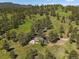 Picturesque aerial view of a stone home surrounded by green meadows and forest, blending with the natural landscape at 3800 Lakota Rd, Indian Hills, CO 80454