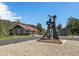 Charming exterior featuring an art sculpture, gravel yard, mature trees, and green home with red roof at 3800 Lakota Rd, Indian Hills, CO 80454