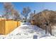 Snowy driveway leads to detached garage, framed by a wooden fence and mature trees offering privacy at 2918 Ames St, Wheat Ridge, CO 80214