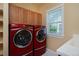 Bright laundry room featuring red washer and dryer units, upper cabinets and a window at 8171 E 33Rd Ave, Denver, CO 80238