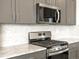 Modern kitchen featuring stainless steel gas range, microwave, sleek gray cabinetry, and stylish backsplash design at 6050 Hourglass Dr, Brighton, CO 80601