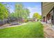 Spacious backyard featuring a trampoline, playground, mature trees, and green grass for play and relaxation at 5200 W Rowland Ave, Littleton, CO 80128