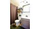 Compact bathroom with a toilet, sink, vanity, and storage shelves, complemented by a brown shower curtain at 9512 W Ontario Dr, Littleton, CO 80128