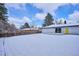 Spacious backyard with a snow-covered lawn, wooden fence and a charming white-brick house with a bright yellow door at 3091 S Krameria St, Denver, CO 80222