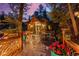 Exterior of home with expansive deck featuring dining, landscape lighting, and seating nestled in a forest setting at 30264 Upper Bear Creek Rd, Evergreen, CO 80439