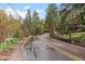 Wet road leading to property surrounded by tall trees and a split rail fence at 30264 Upper Bear Creek Rd, Evergreen, CO 80439
