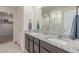 Bathroom with double sinks, granite countertop, mirrors, and a shower at 7414 Blue River Ave, Frederick, CO 80530